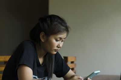 The young woman intently uses a smartphone in the kitchen.