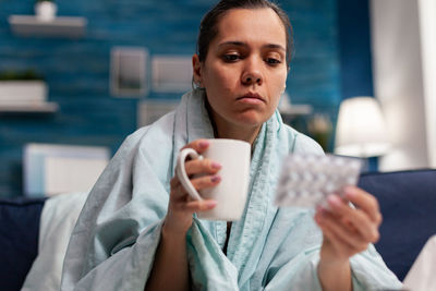 Young woman holding coffee cup with medicine at home