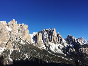 Low angle view of snowcapped mountains against clear blue sky