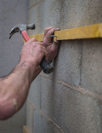 Cropped hand of man hammering nail in wood on wall at home