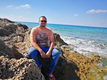 Portrait of young man sitting on rock at beach