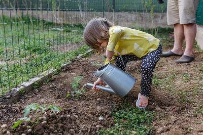 Side view on baby watering seedling from metal watering can in the garden