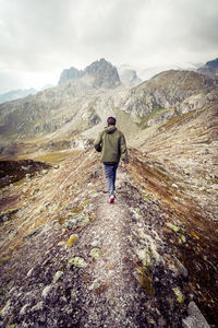 Rear view of man walking on mountain against sky