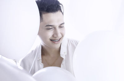 Close-up of smiling young man with balloons against white background