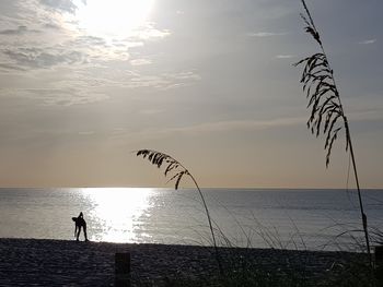 Silhouette person exercising at beach against sky during sunset