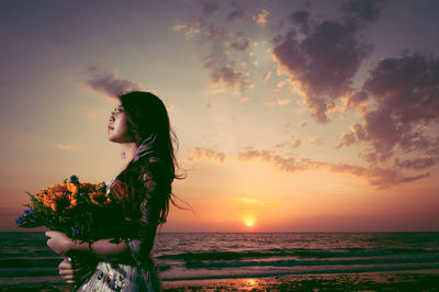 Full length of woman with flowers standing on sea shore against sky