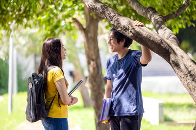 A couple of thai high school students smile while going through the woods with a book in their hands