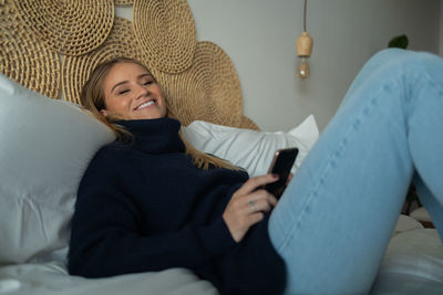 Young woman using mobile phone while sitting on bed at home