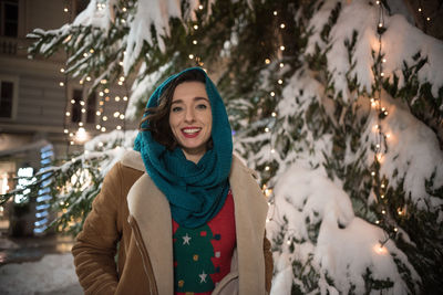 Portrait of woman standing against illuminated tree during winter