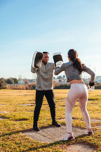Woman boxing with instructor on land against sky