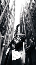 Low angle view of woman with arm raised standing amidst buildings in city