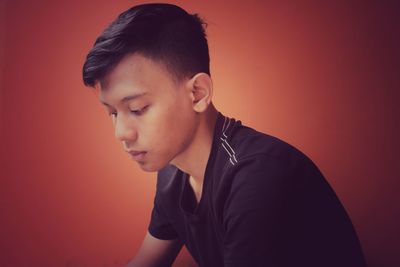 Thoughtful teenage boy looking down while sitting over red background