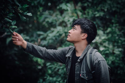 Young man looking away while standing against plants