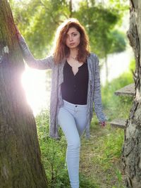 Portrait of young woman standing on tree trunk