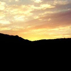 Silhouette landscape against cloudy sky at sunset