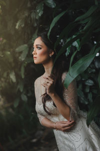 Young woman looking away while standing against plants