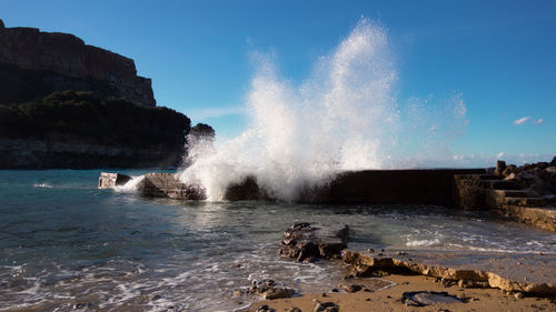 Waves splashing on rocks at shore against sky