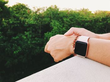 Cropped hands of man wearing smart watch on railing against trees during sunset