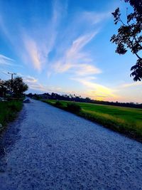 Road amidst field against sky during sunset