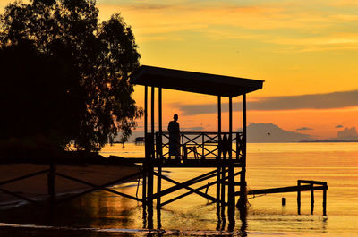 Silhouette man by tree against orange sky