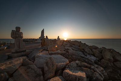 Rocks on beach against sky during sunset