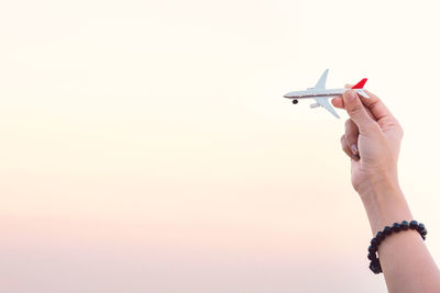 Cropped hand of woman holding toy airplane against clear sky