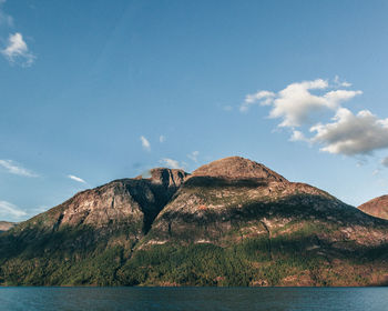 Shadow and sun over a rocky and green mountain and fjord glacier water 