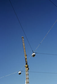 Low angle view of crane and cables against clear blue sky