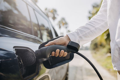 Hand of man charging electric car on roadside at station