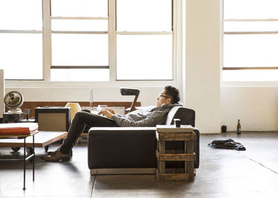 Side view of businessman using laptop while reclining on sofa at office