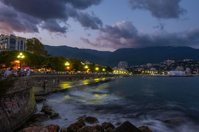 Illuminated city by sea against sky at night