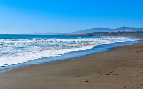 Beautiful tranquil sandy beach with gentle waves rolling in amidst mountain background