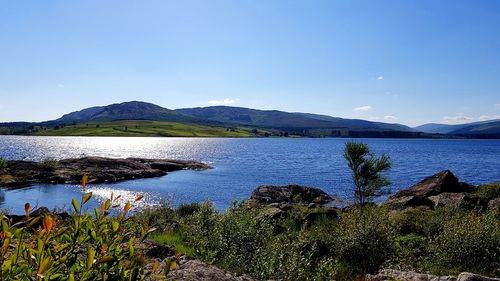 Scenic view of lake and mountains against clear blue sky