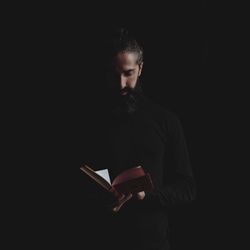 Young man reading book against black background