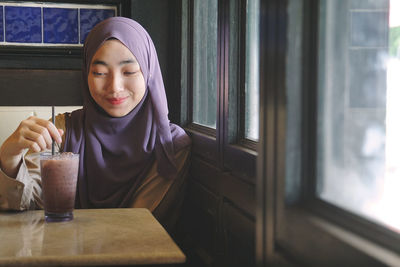 Smiling young woman wearing hijab while having drink at restaurant
