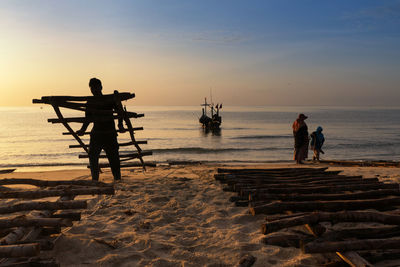 Silhouette people standing on beach against sky during sunset