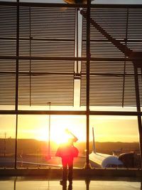 Silhouette woman standing by airplane window against sky during sunset