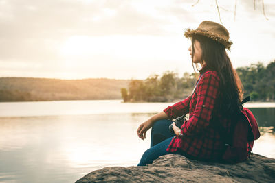 Side view of young woman sitting against sky