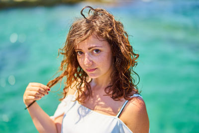 Portrait of young woman standing against sea during sunny day