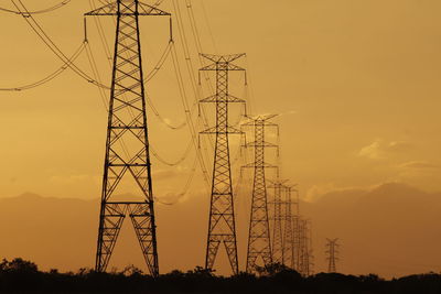 Low angle view of electricity pylon against sky during sunset