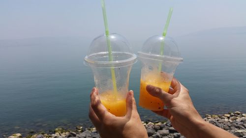 Cropped hands holding slushies against lake tiberius during foggy weather