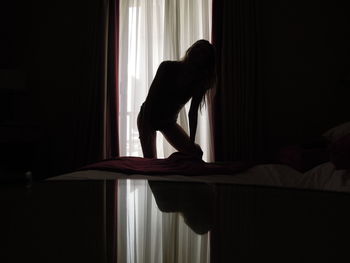 Silhouette woman by bed against curtain in bedroom