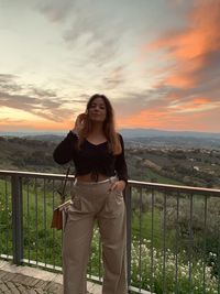 Young woman photographing while standing against sky during sunset