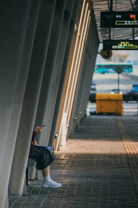 Low section of woman using phone while sitting at railway station