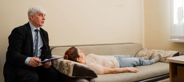 Full length of man holding woman sitting on sofa