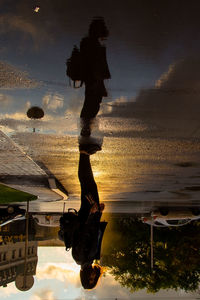 Low section of man with reflection in puddle against sky