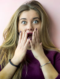 Portrait of surprised young woman against pink background