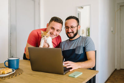 Two men and a cat looking at a laptop.