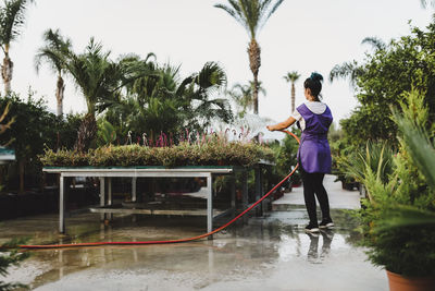 Rear view of female garden center owner watering potted plants