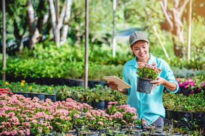 Portrait of smiling woman standing by flower plants